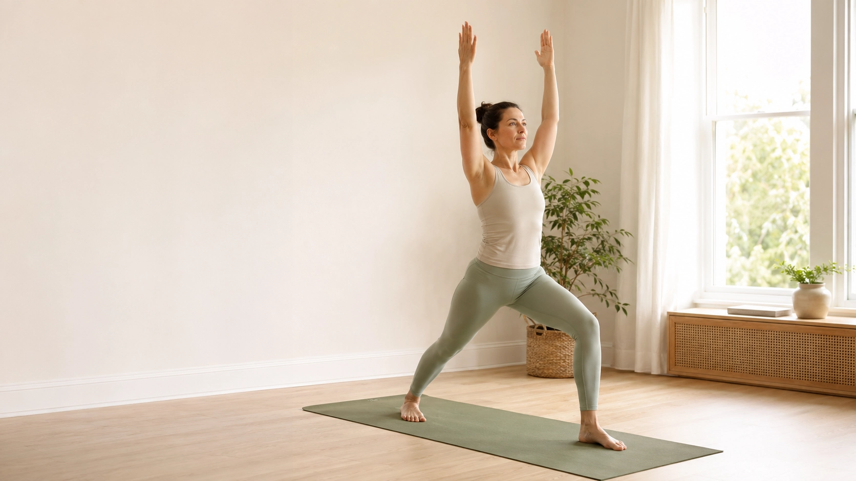 Woman practising a beginner-friendly Warrior I yoga pose at home on a sage green mat